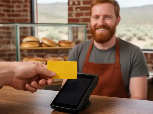 Bearded bakery owner in a rust apron smiling behind a counter as a hand holds a yellow card to a terminal